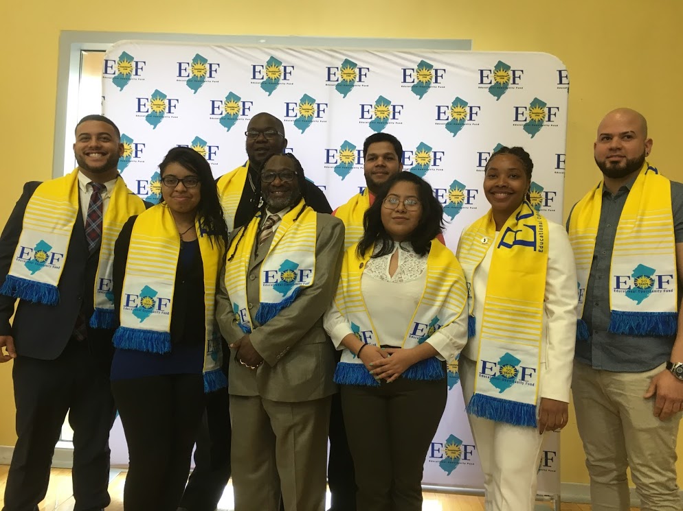 Several Students standing in front of an EOF patterned background. They are also wearing EOF styled Stole