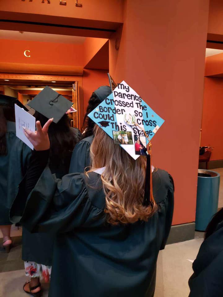 The back of a student walking for graduation. On top of the cap it is personally styled by the student and it reads " My parents crossed the border, so that I could cross this stage"