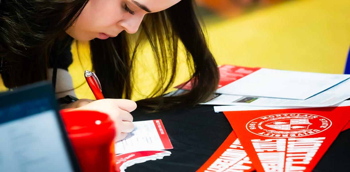 Student completes a form at a Montclair State University information table during a college transfer event.