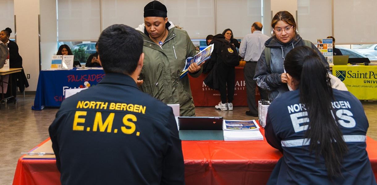 Attendees speak with North Bergen EMS representatives at an information table during a college and career event.