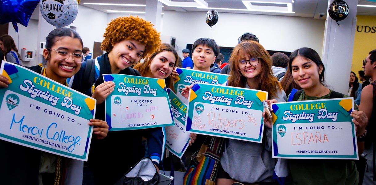 Group of students pose together holding College Signing Day signs announcing plans to attend Mercy College, Rutgers University, and study in Spain.