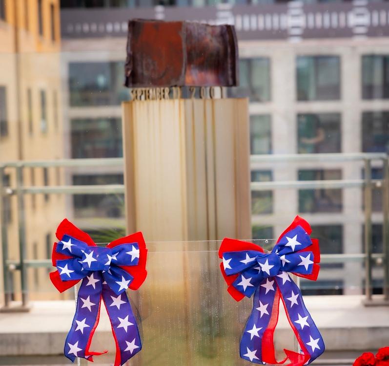 A World Trade Center steel beam serves as a memorial to the victims and heroes of September 11, displayed with patriotic flowers and ribbons during a remembrance observance.