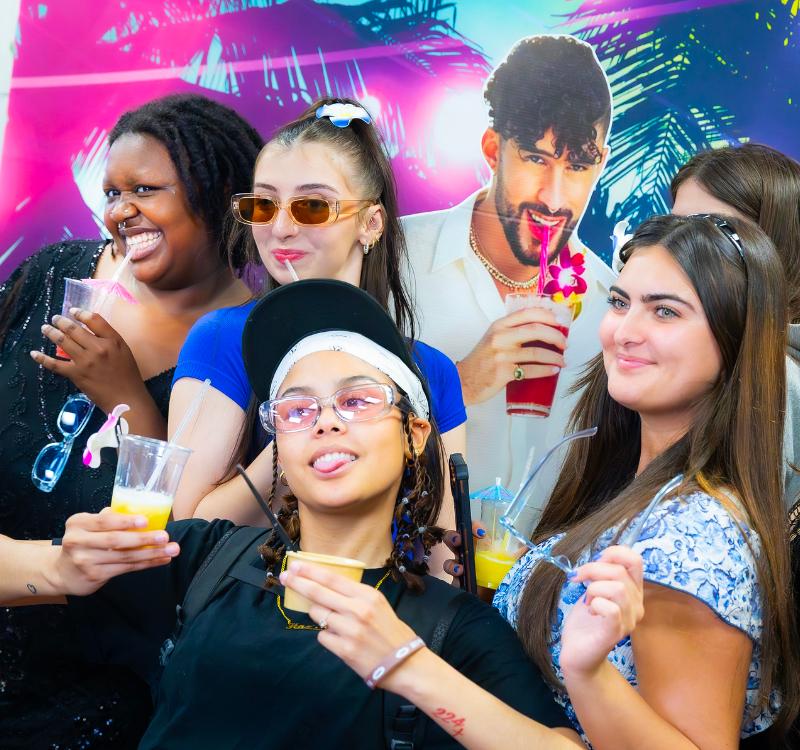 Students pose with tropical-themed drinks in front of a colorful photo backdrop during the HCCC Graduation BBQ celebration.