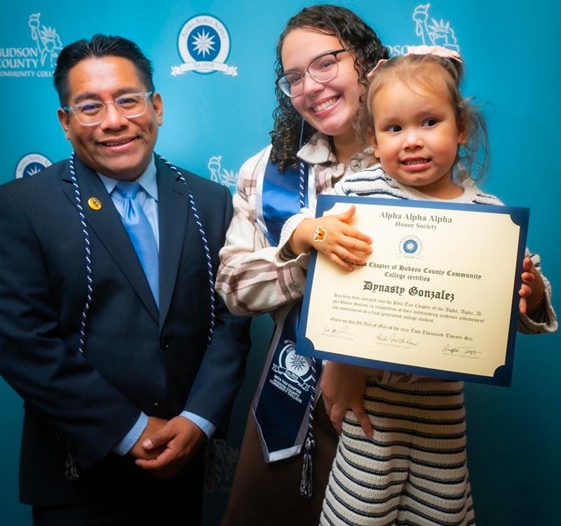 A student celebrates induction into the Alpha Alpha Alpha Honor Society with family members during an HCCC recognition event, marking academic achievement and perseverance.