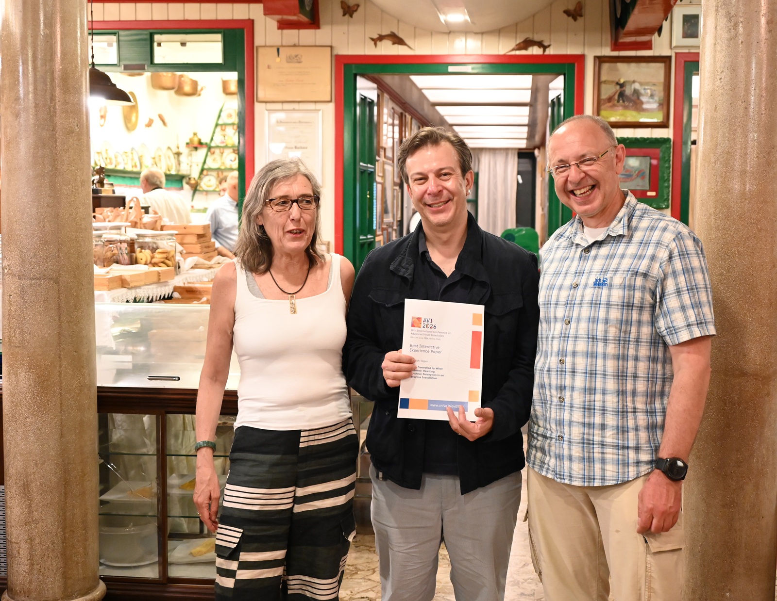 Dr. Antonella De Angeli (left), Professor Teipen (center), and a colleague pose together at an awards event. Professor Teipen holds an AVI award certificate recognizing achievement in interactive experience design.