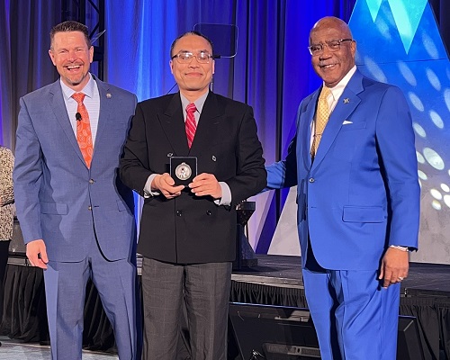 Prof. Li holding AACC 2023 Dale P. Parnell Distinguished Faculty Recognition award with AACC Board of Directors Chair, Dr. Joseph Schaffer to his left and AACC President and CEO, Dr. Walter G. Bumphus to his right.